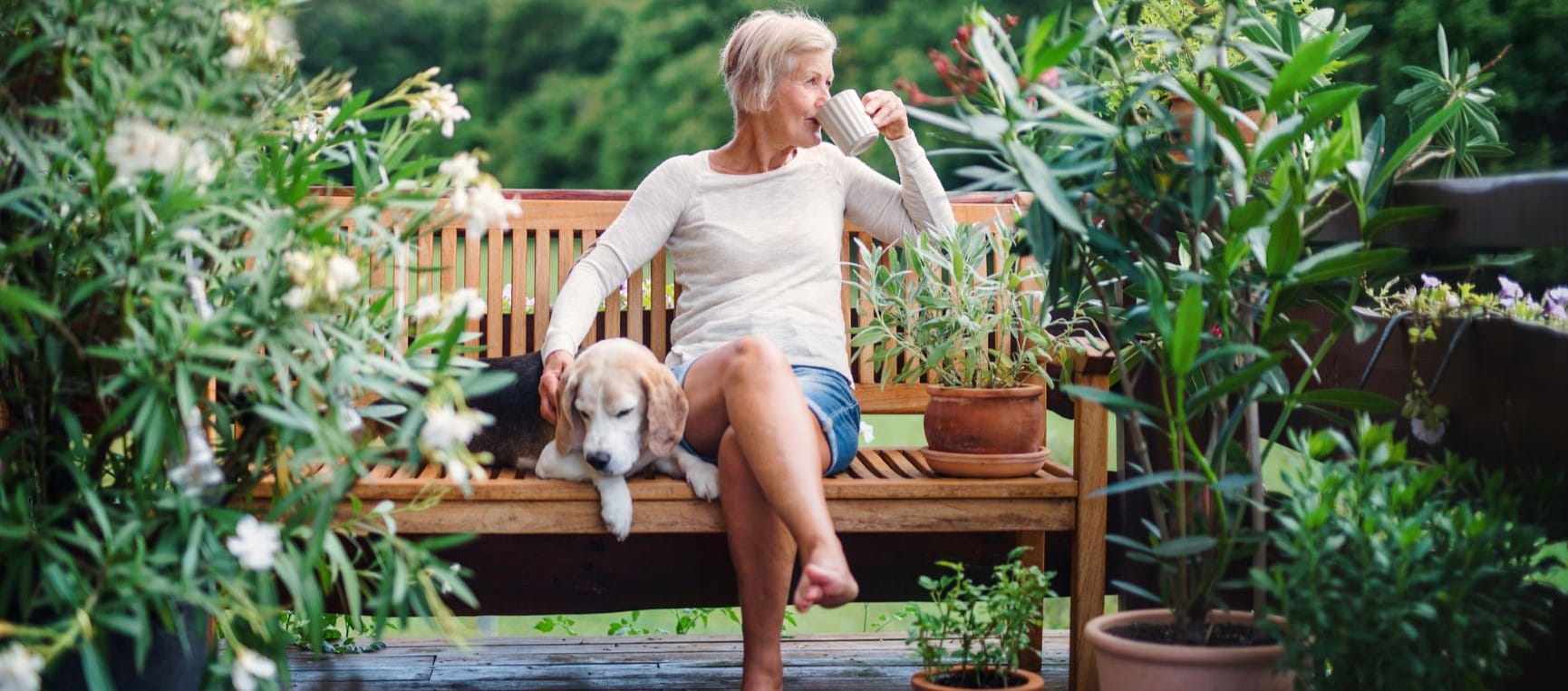 Woman drinking a coffee on a bench with a dog