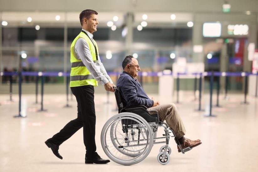  airport worker pushing a mature man in a wheelchair at the airport