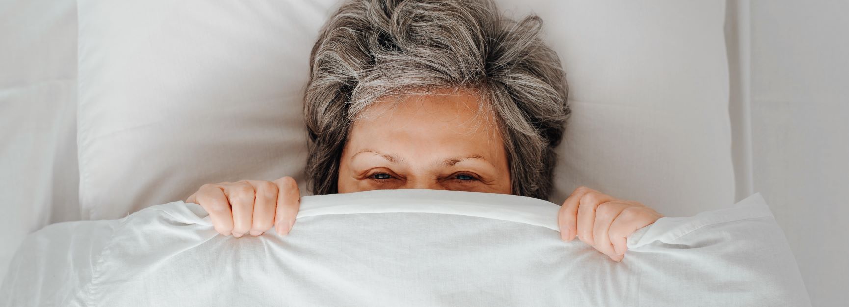 Woman in bed with the covers pulled up over her mouth