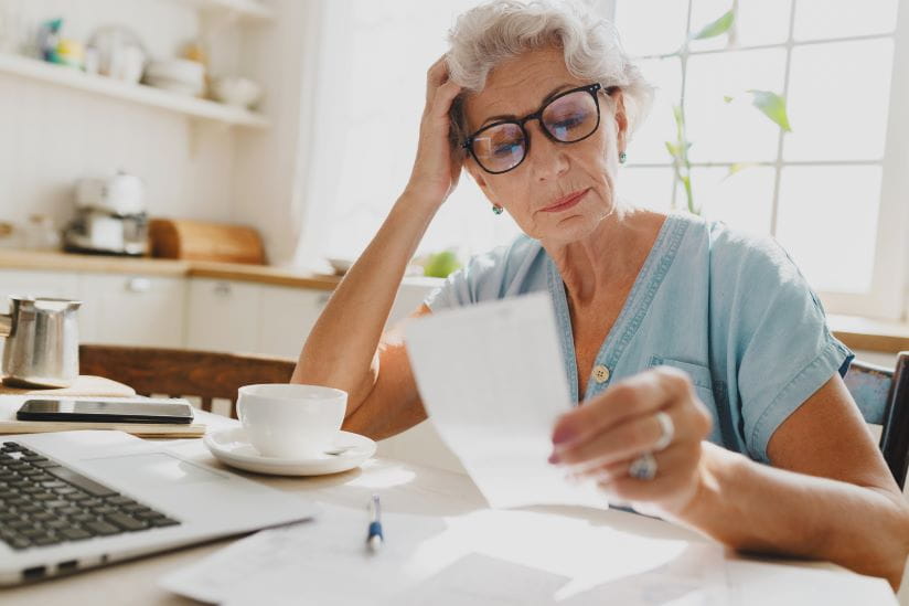 Woman looking at receipts at her kitchen table with her laptop
