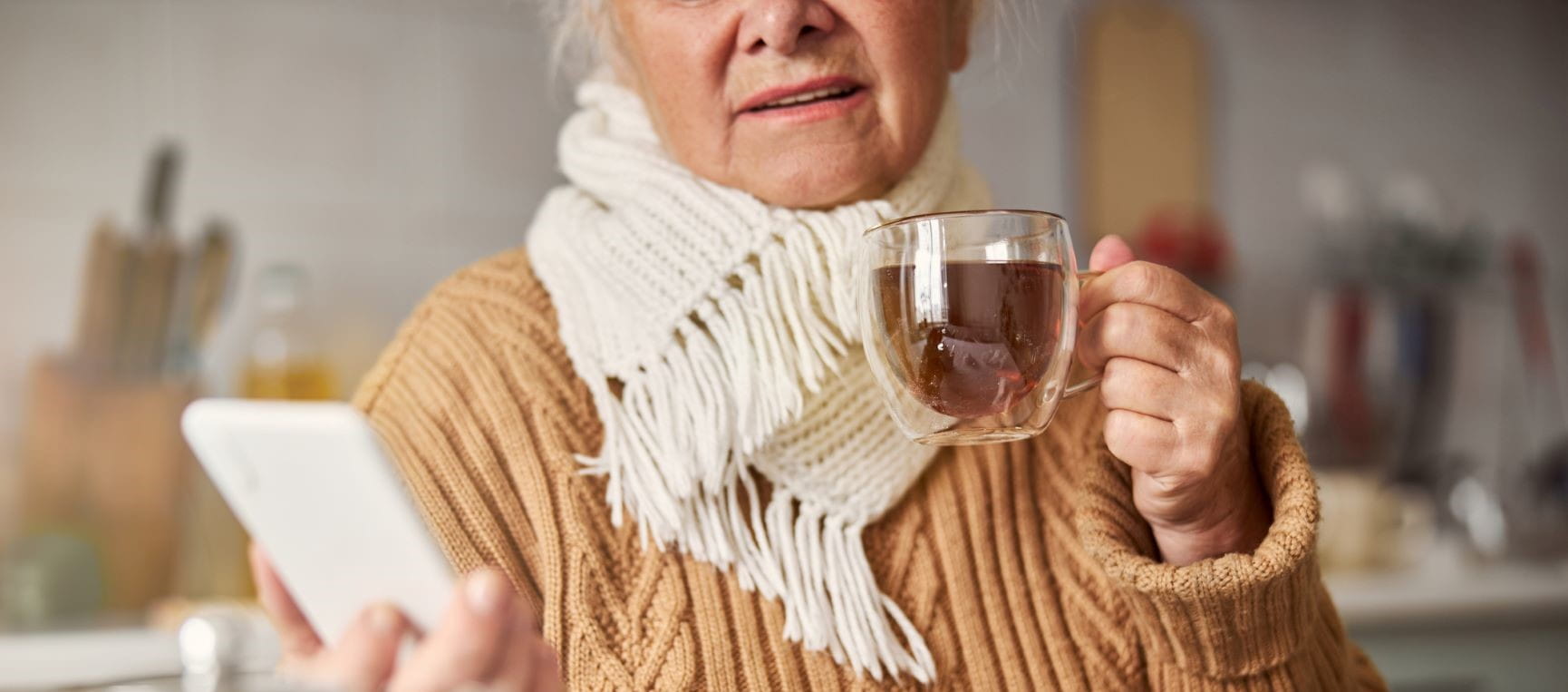 Lady keeping warm with a scarf, jumper and tea while checking her phone
