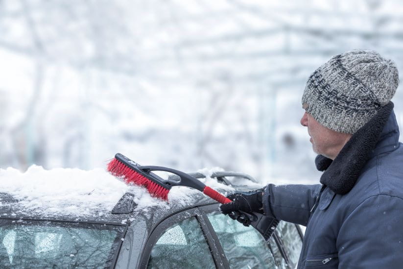 man trying to brush the snow off the top of the car