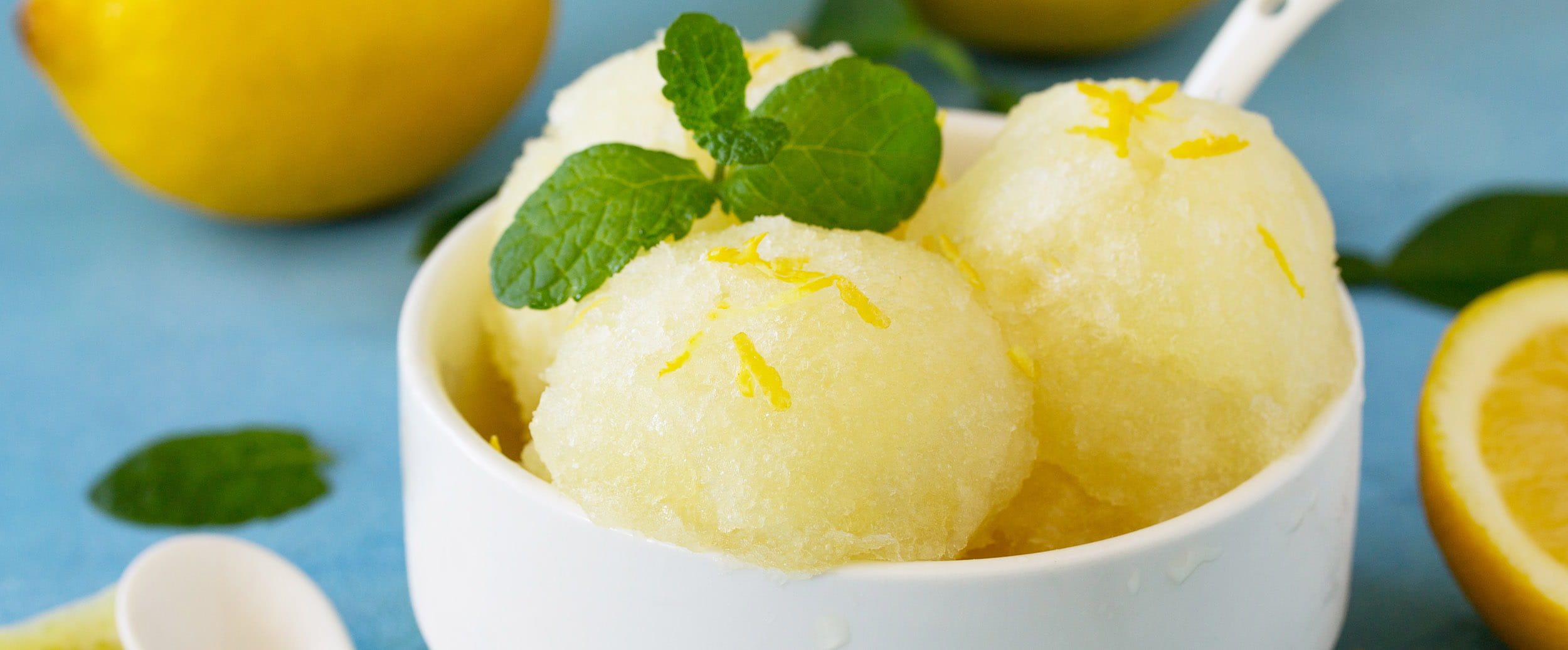 scoops of lemon sorbet in a bowl surrounded by cut up lemons