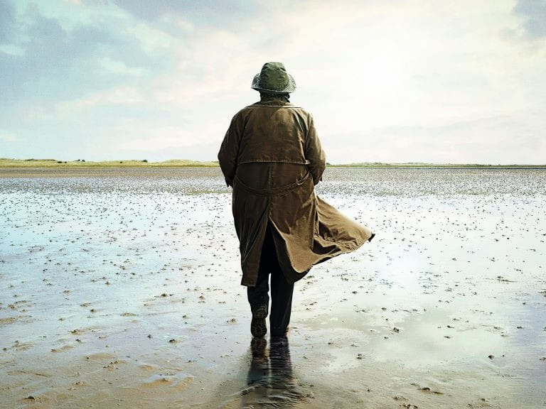 Vera with her back to the camera walking along the sand