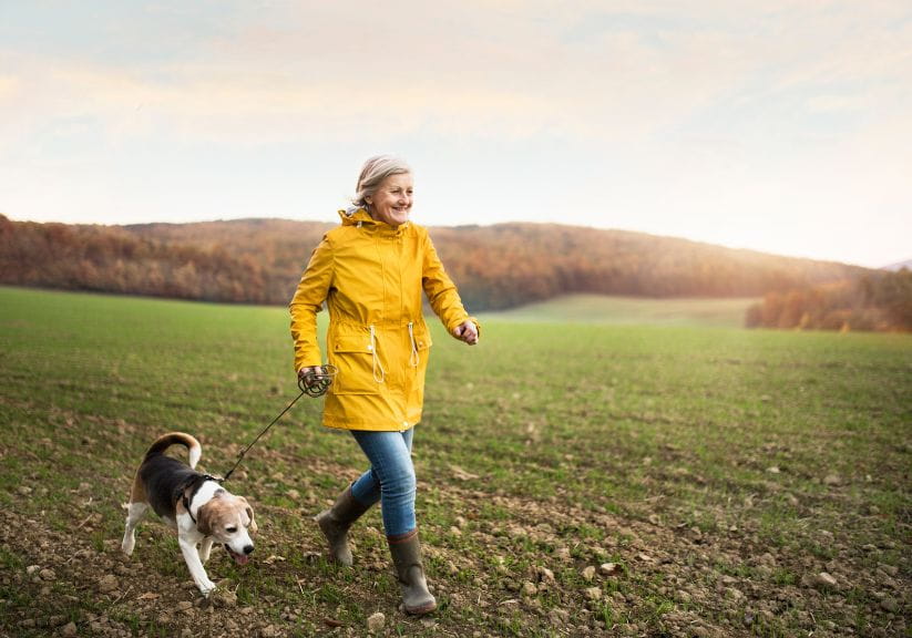 A woman in a rain mac walks her dog outside