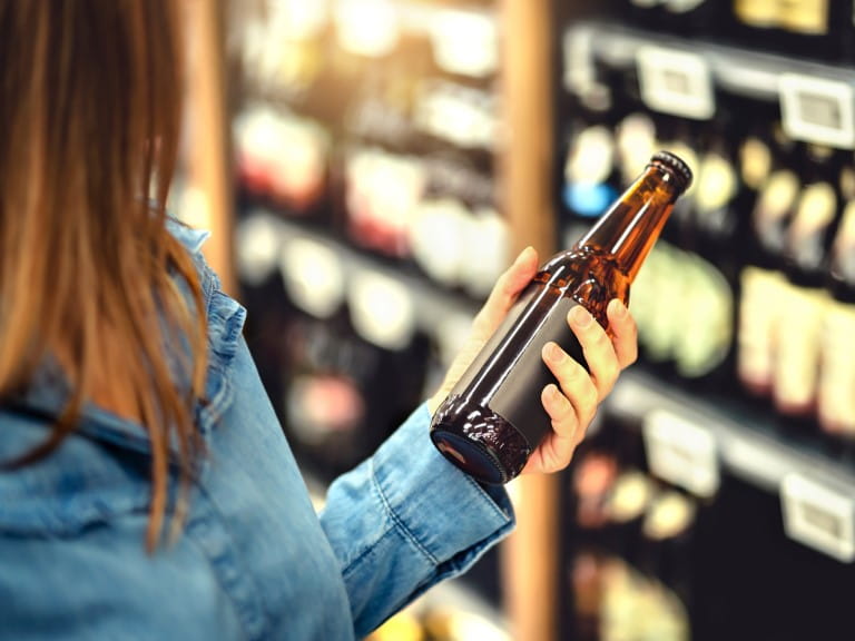 A woman examining a beer in a supermarket