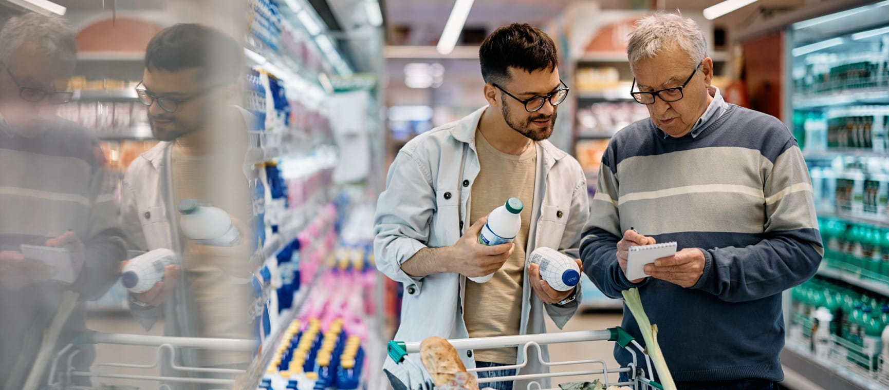 Young man and his senior father going through shopping list while buying in supermarket