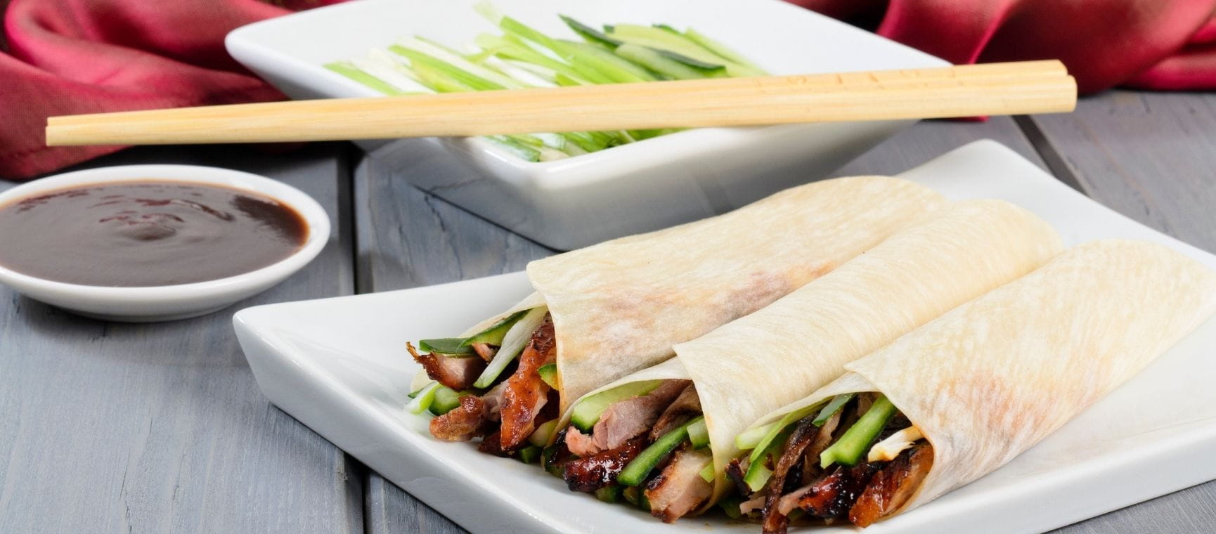 three rolled up Chinese style duck pancakes on a table with chopsticks