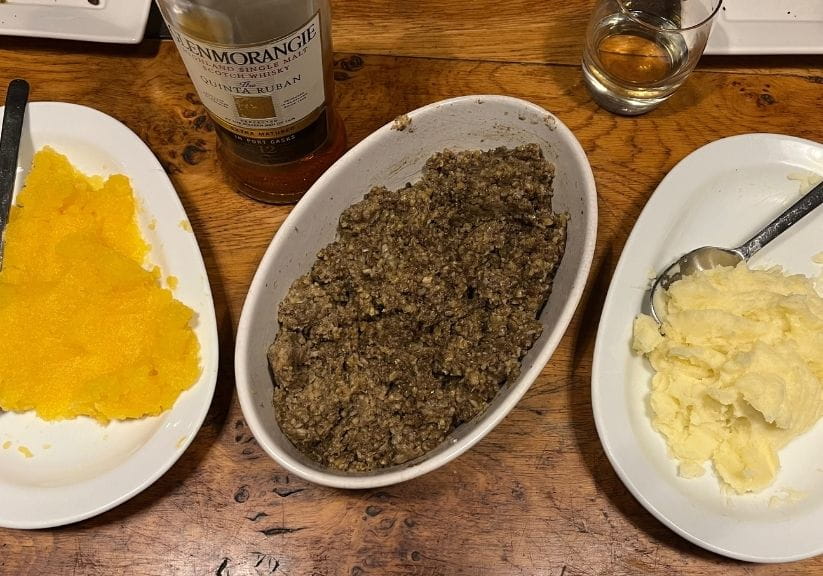 a bowl of cooked haggis on a table with swede and potatoes in separate bowls