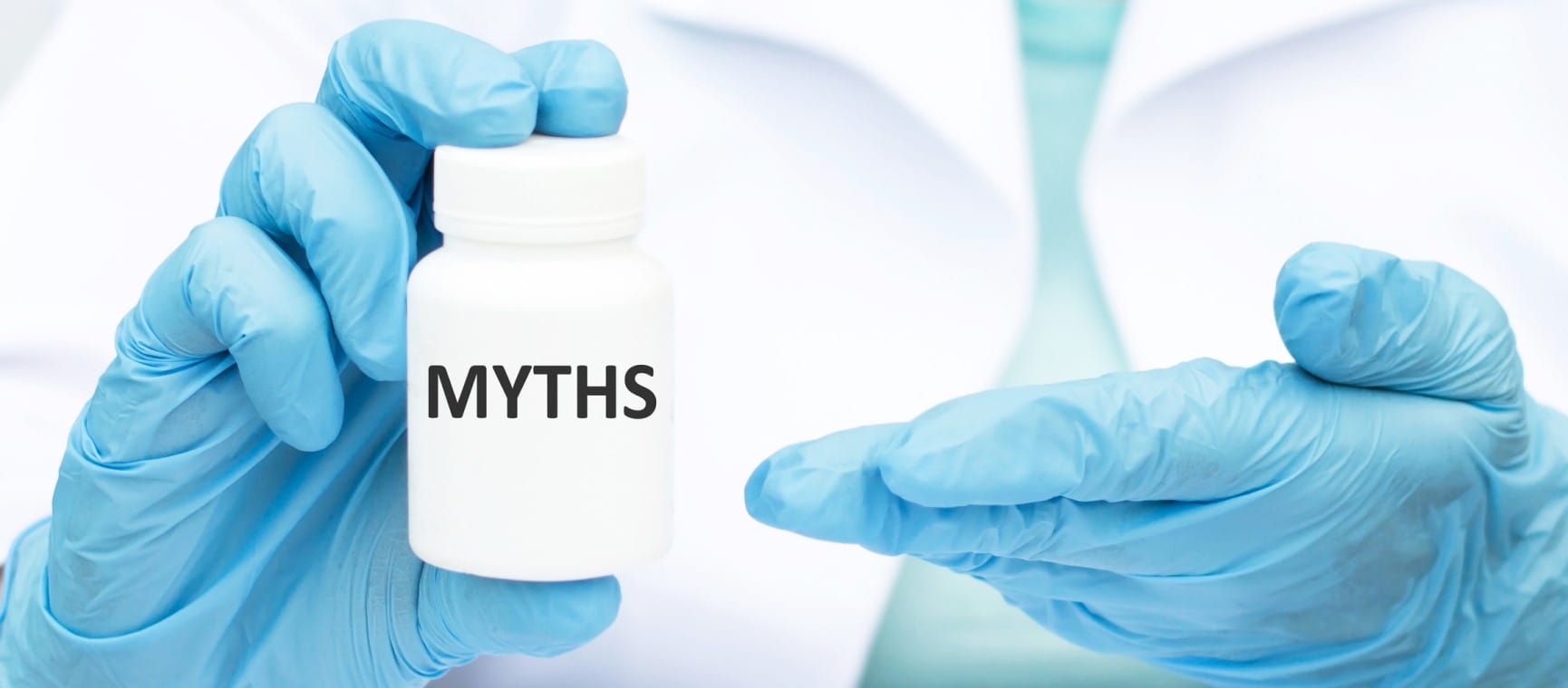 Hands in blue medical gloves holding a pill bottle labelled "Myths"