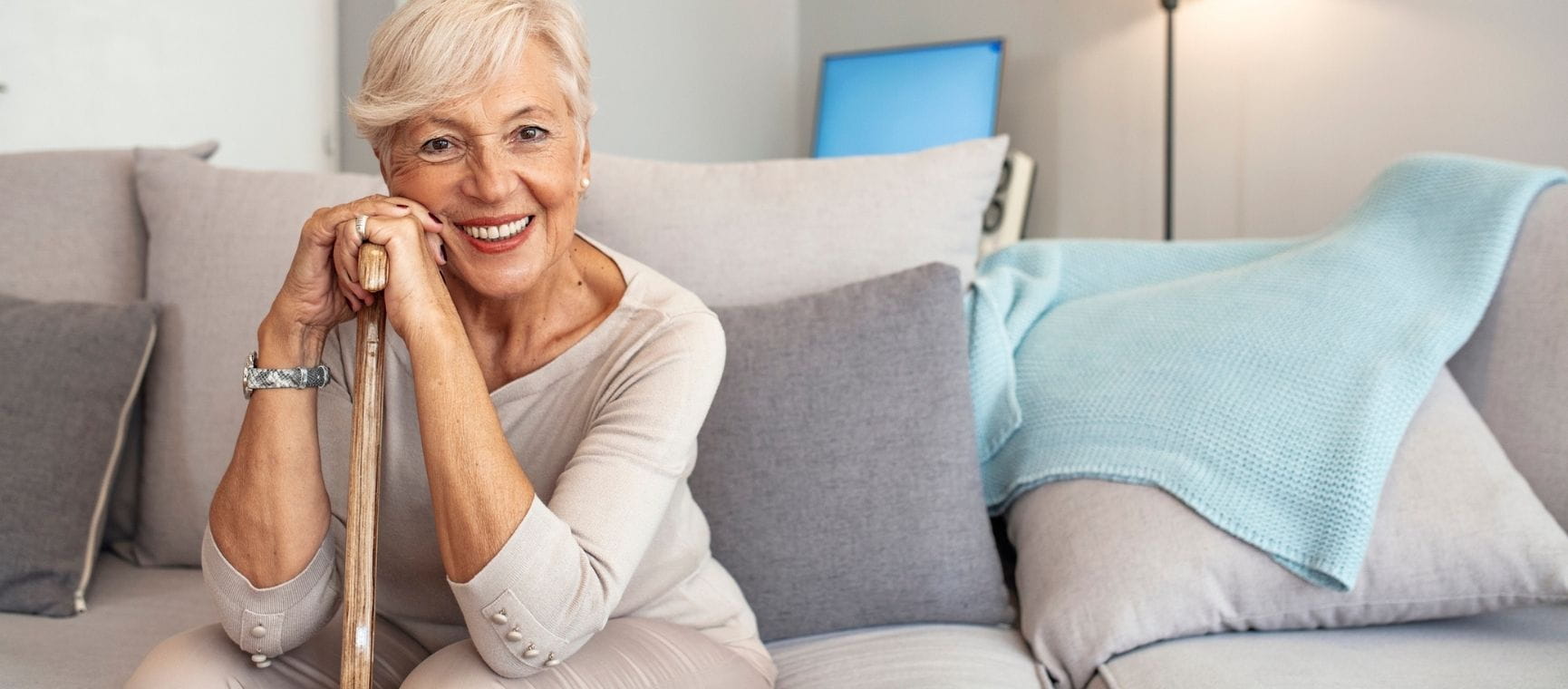 A woman sat on a sofa smiling and holding a walking stick