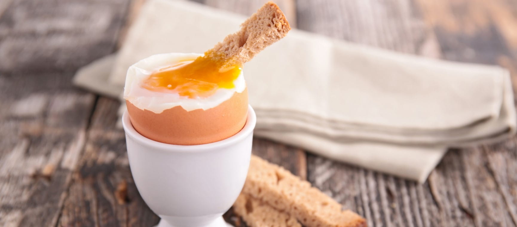 A boiled egg with the top removed and a runny yolk, with a small piece of bread dipped in