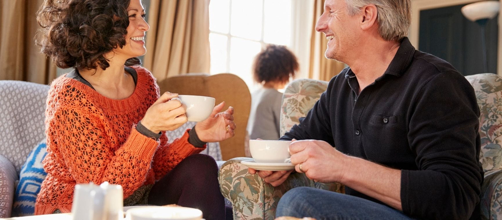 A couple at a coffee shop sitting on sofas sharing coffee and smiling