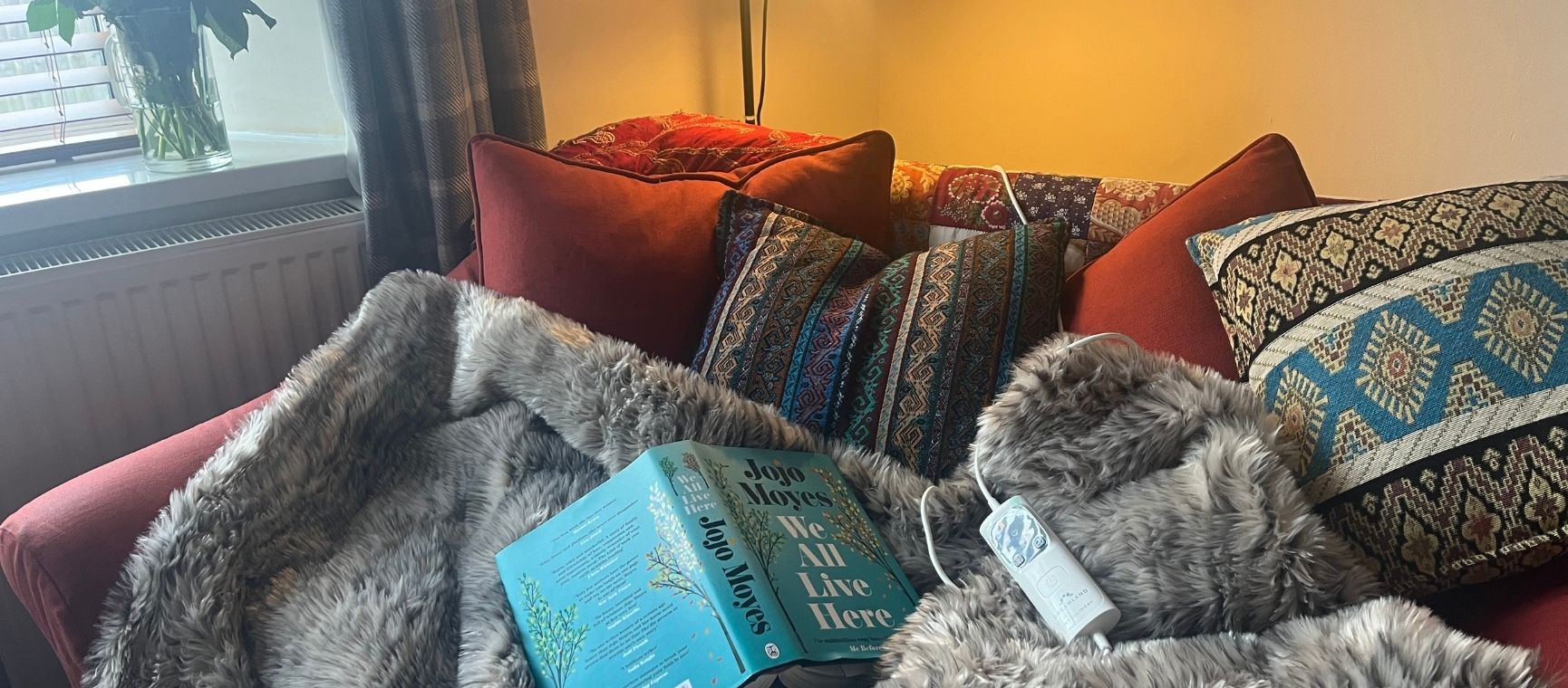 a furry electric throw on a sofa with cushions and a book on top of it