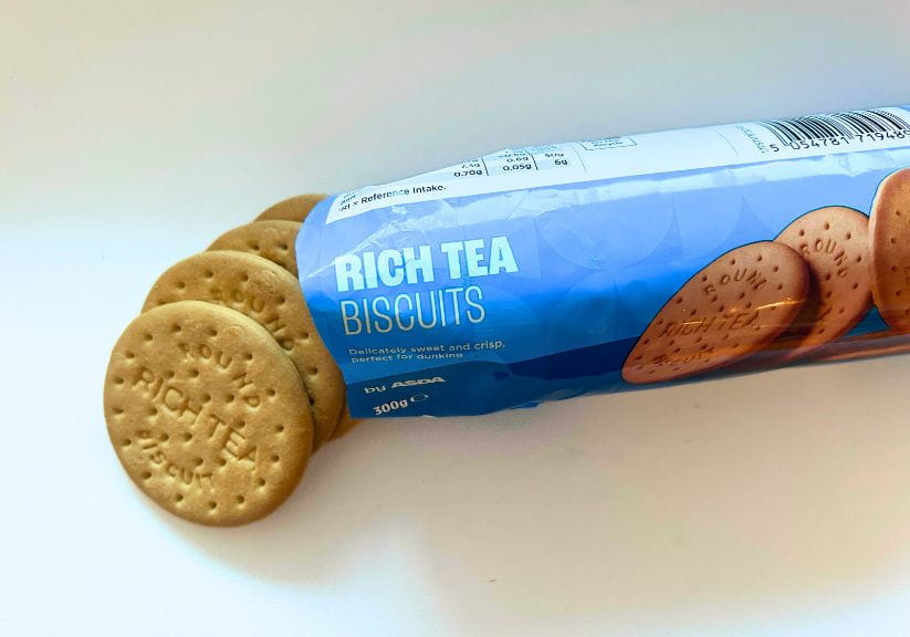 A packet of Rich Tea with some loose biscuits on a white background