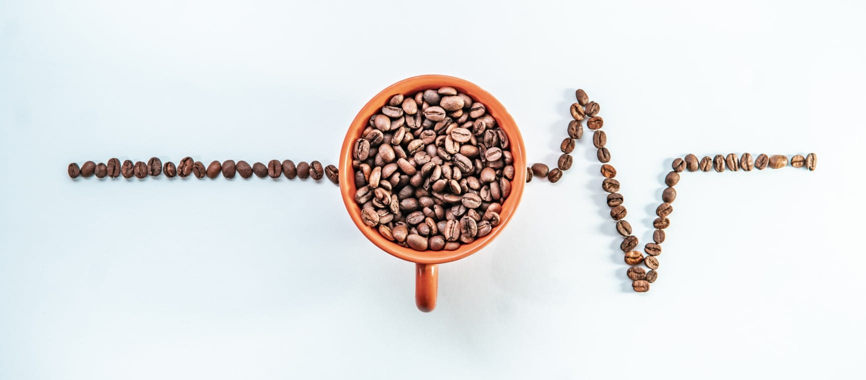 A mug full of coffee beans, with more beans laid out to appear like the readout on an EKG machine