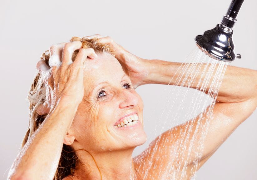 A mature woman washes her hair in the shower