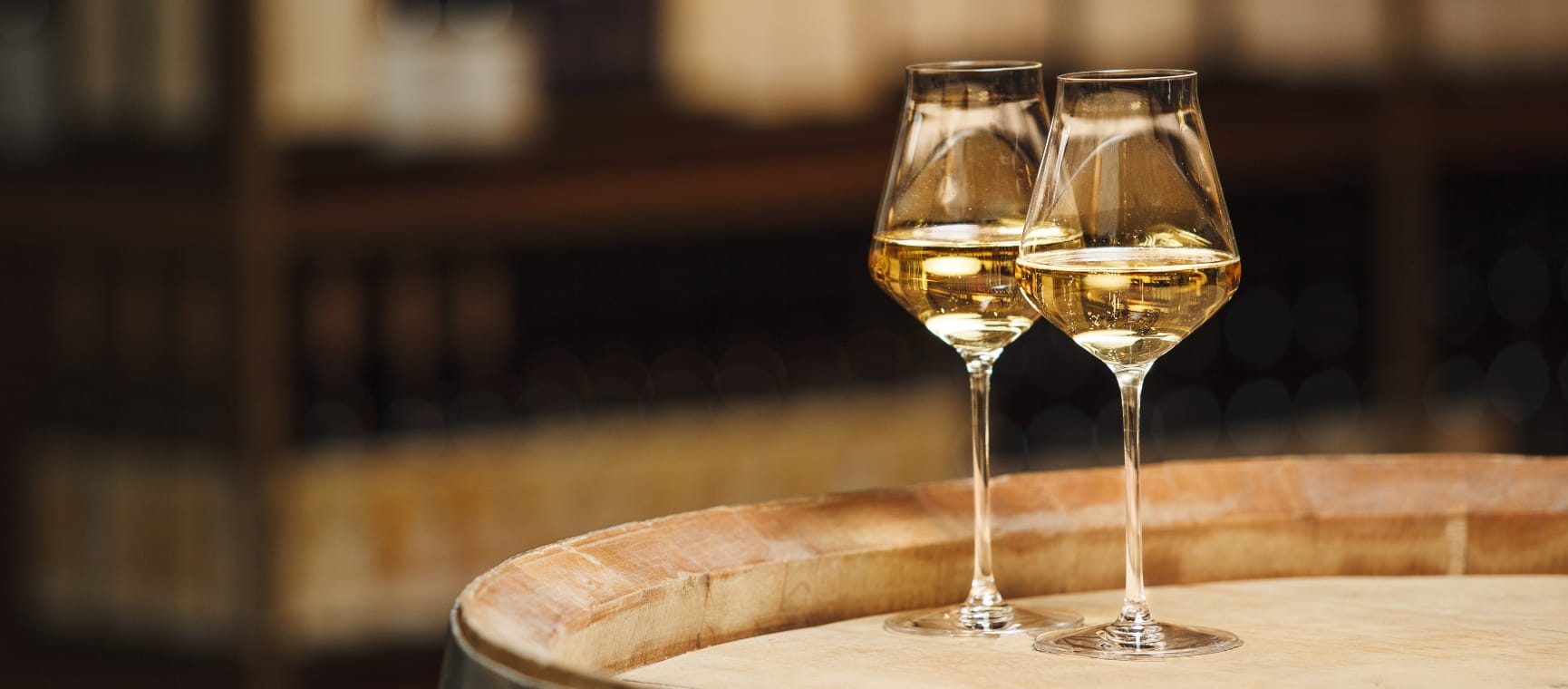 Two glasses of white wine atop a barrel in a wine cellar