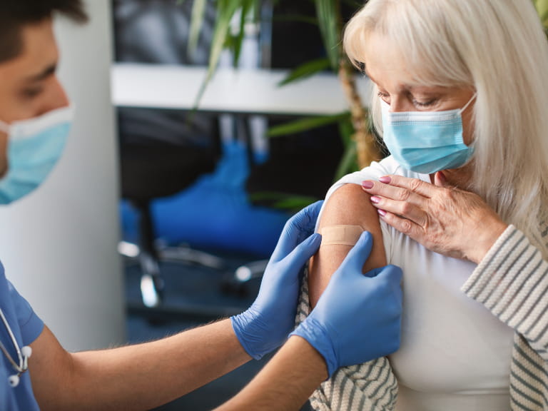 A doctor placing a plaster on a senior woman's arm after receiving a vaccine