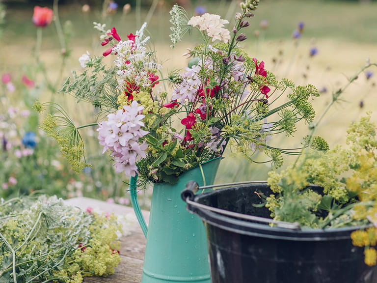 A flower arrangement in a green jug next to a bucket of cut flowers