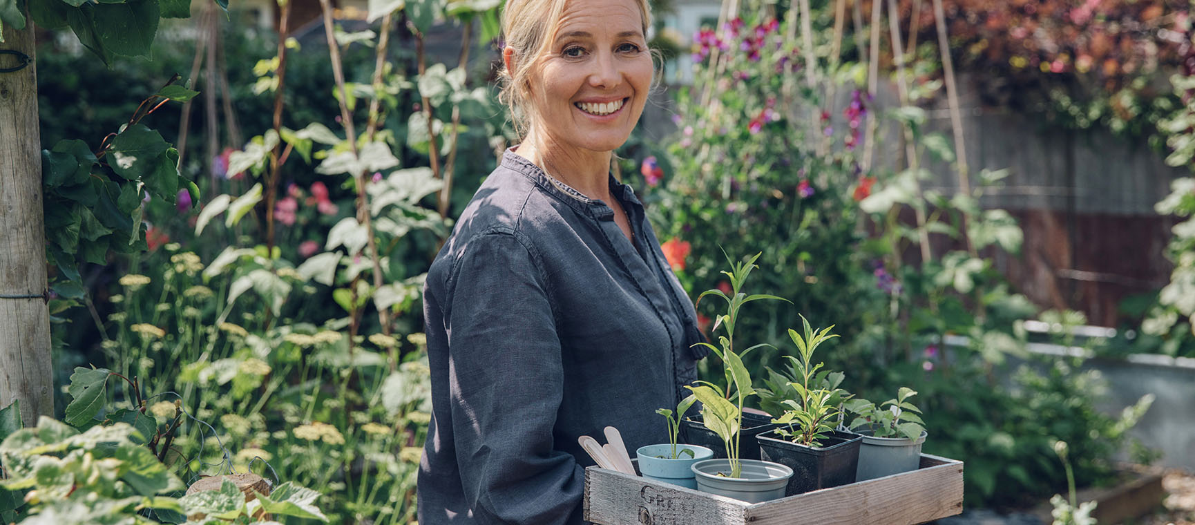 Author and gardener Clare Foster in a cut garden holding a wooden tray with potted seedlings