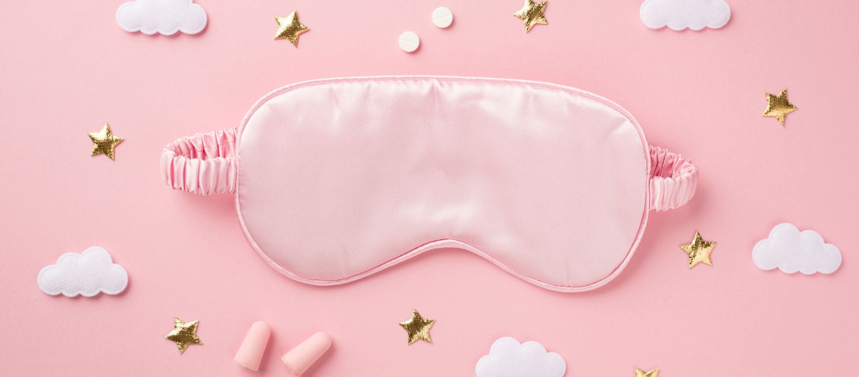 A pink sleep mask against a pink background with clouds