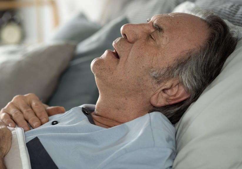 An older man snoring in bed