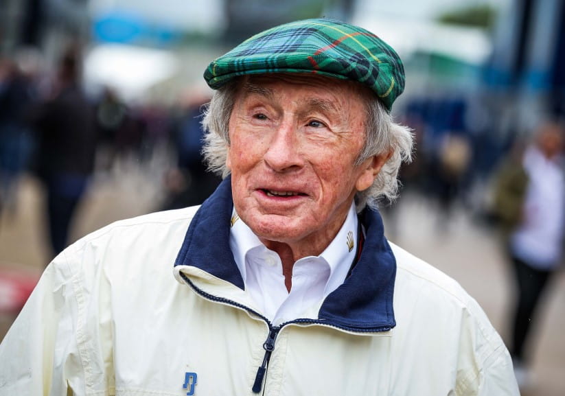 Sir Jackie Stewart in a white jacket and flat cap