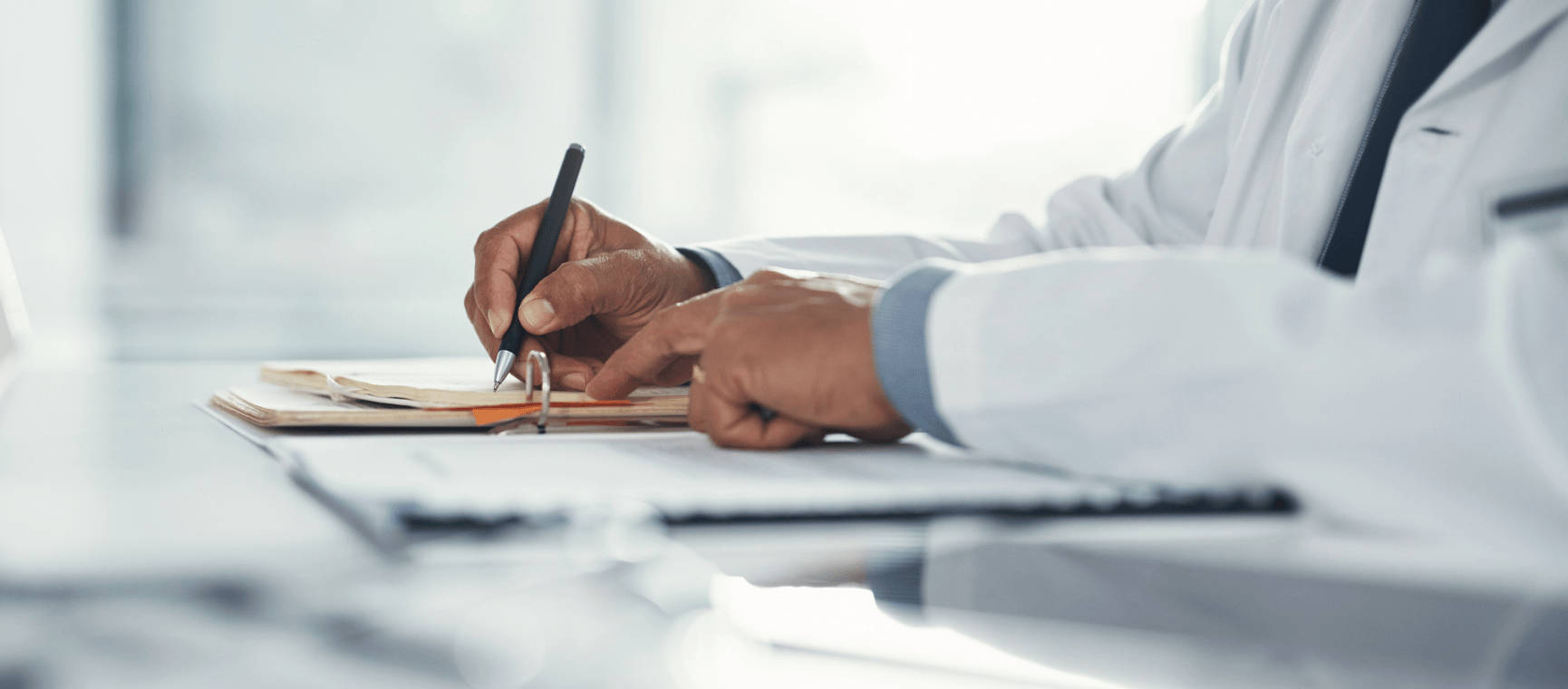 A close up of a man in a white coat writing medical notes