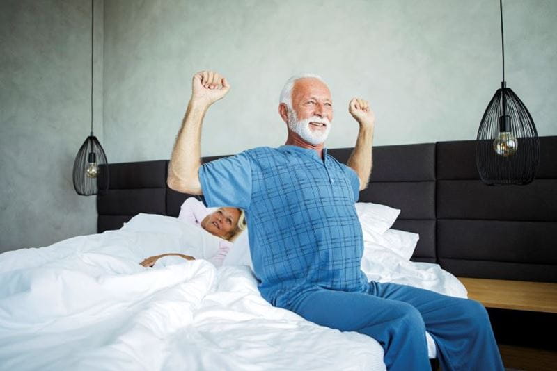 Man sat on the edge of his mattress stretching his back out