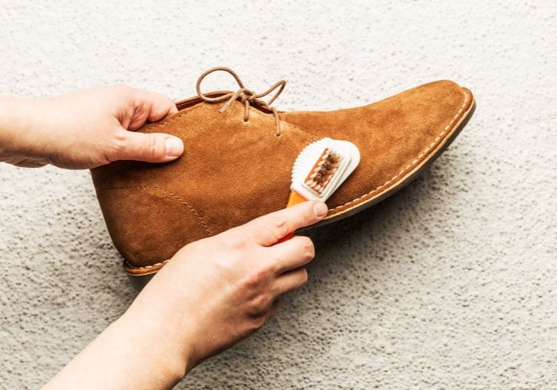 A person cleaning suede desert boots with a suede brush