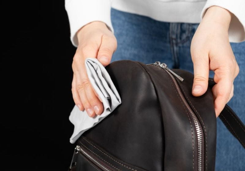 A person cleans a leather backpack with a soft cloth