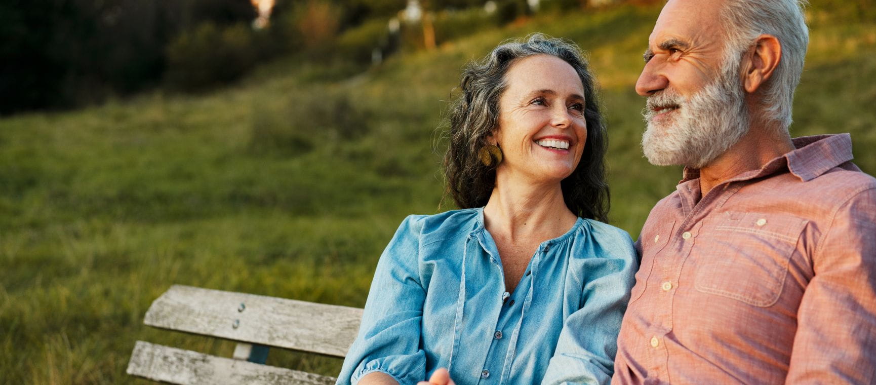 An older couple sat on a bench looking happy, away from the camera