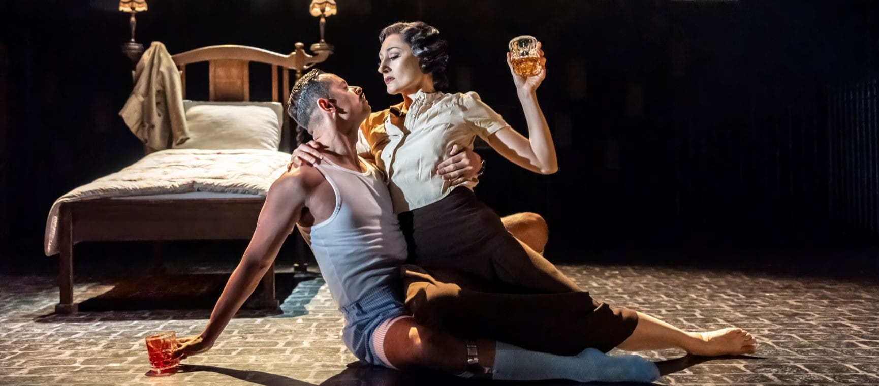 Two characters sitting dramatically on the floor in front of a bed