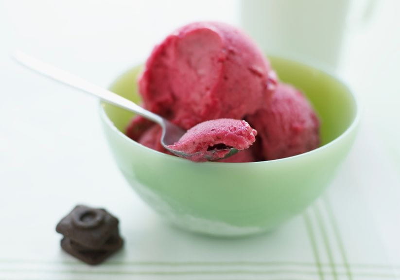 Raspberry sorbet in a green bowl with a spoon and a cookie on a plate