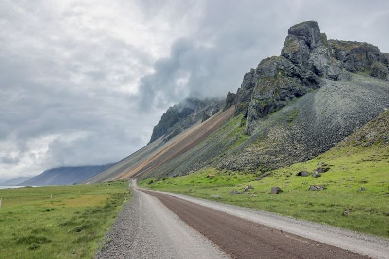 Dirt road at Iceland near Stokksnes cape with mountain peaks covered in clouds