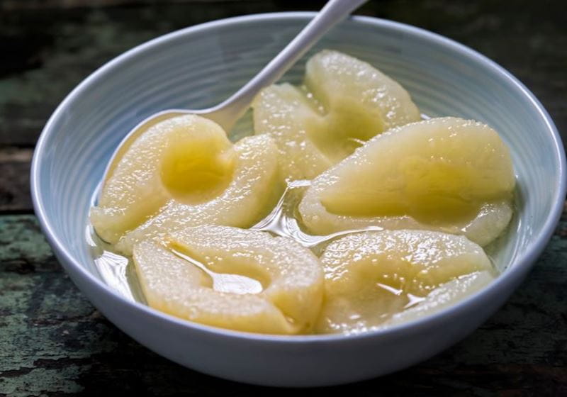 A bowl of tinned pears in juice with a spoon