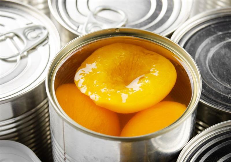 A open can of peaches surrounded by unopened cans