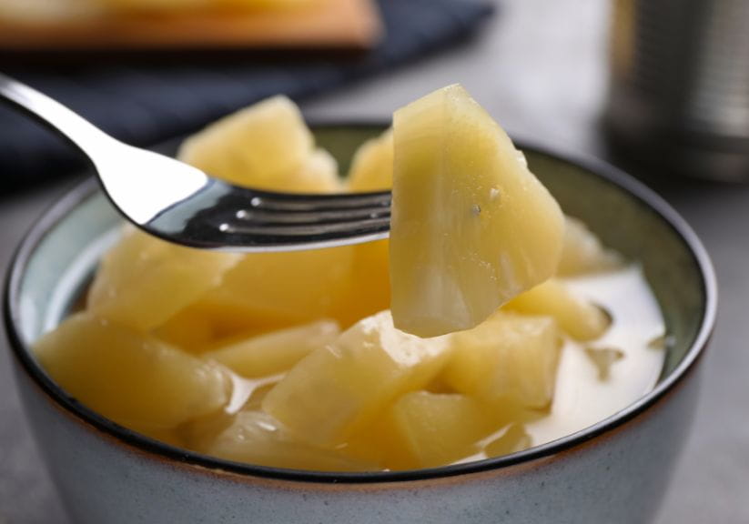 A fork lifting out pineapple chunks from a tin