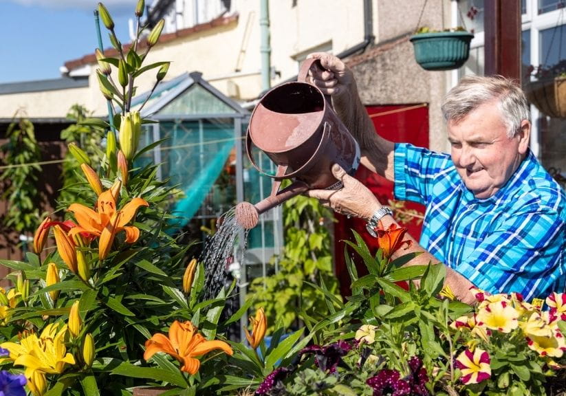 A man watering flowers in his back garden with a watering can