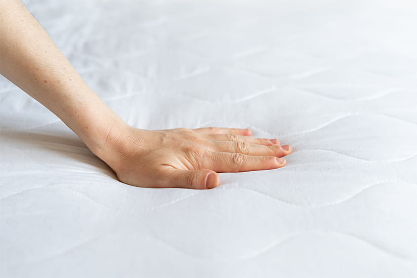 A hand pressing down on a mattress