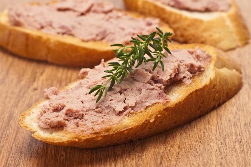 Pâté spread on a slices of French bread, resting on a wooden surface