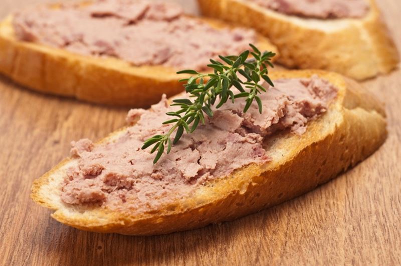 Pâté spread on a slices of French bread, resting on a wooden surface