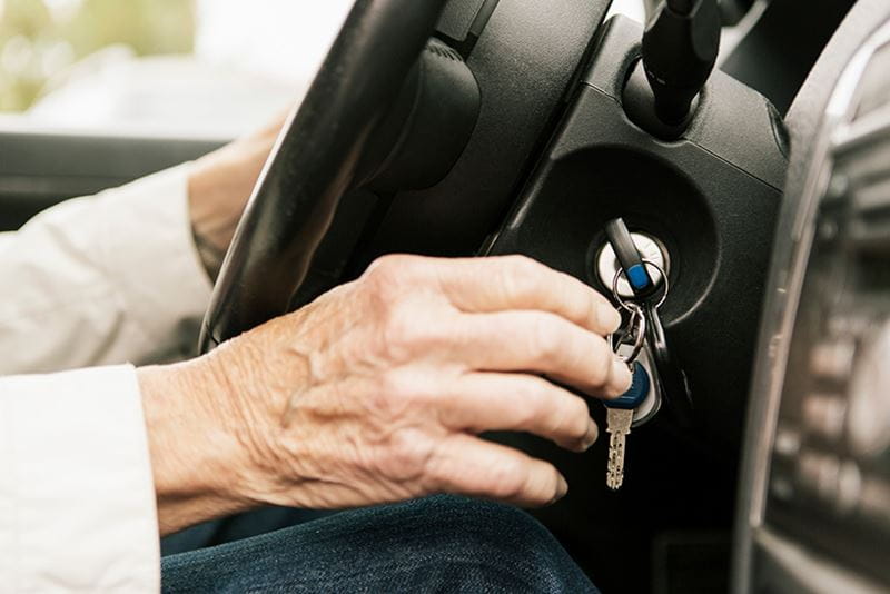 Cropped image of senior woman putting car key in ignition