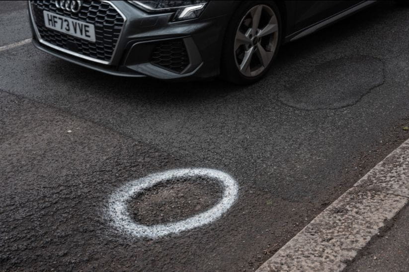A car drives past a pothole marked with white paint