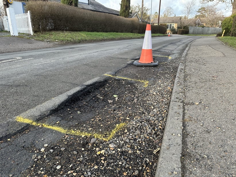 A large pothole marked with yellow paint and an orange traffic cone