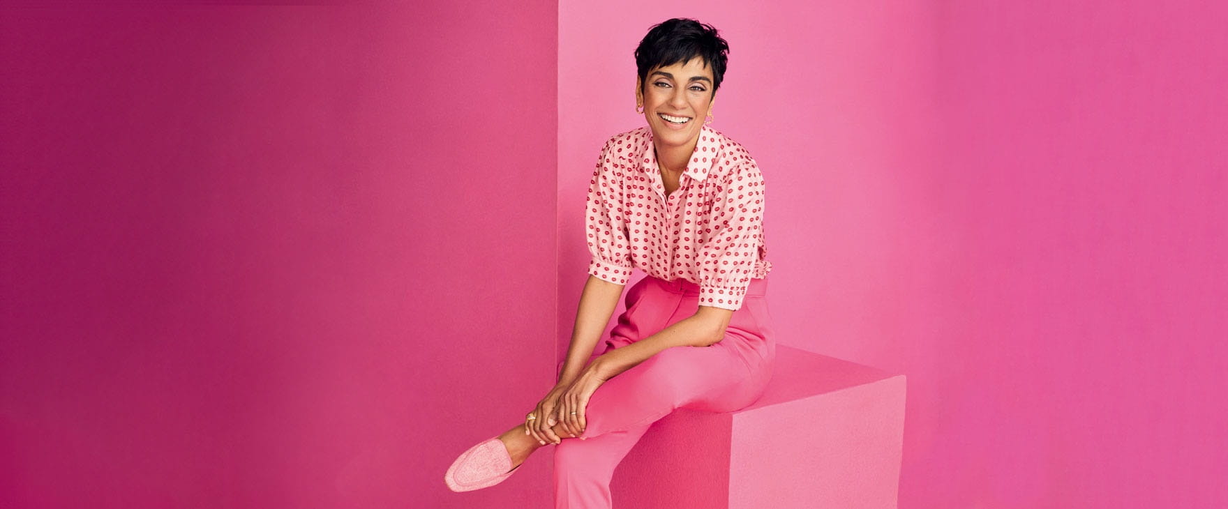 TV presenter Reeta Chakrabarti sat on a block with an all pink background