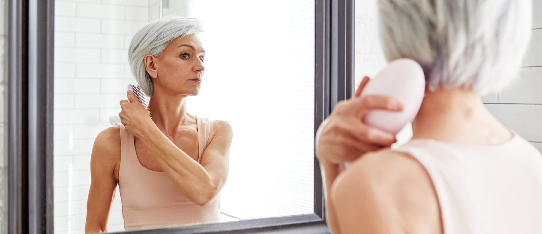 Senior woman brushing straight hair with a hairbrush in bathroom mirror