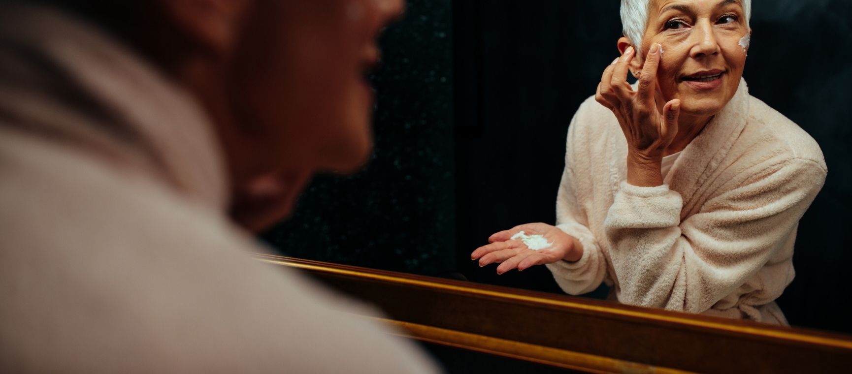 A woman putting moisturiser on in a mirror