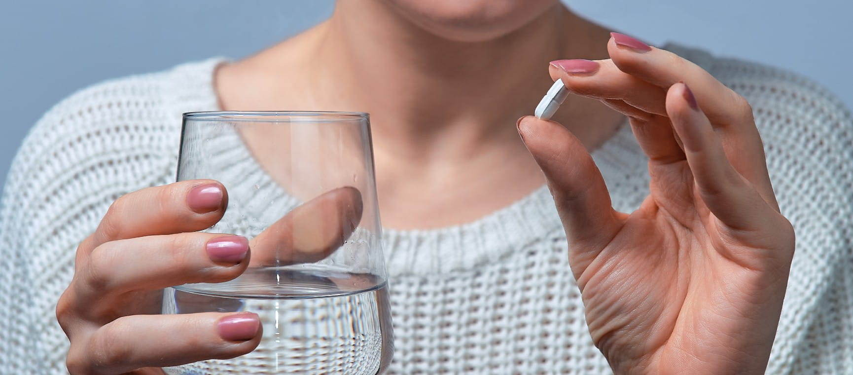 A woman holding a glass of water and an aspirin tablet